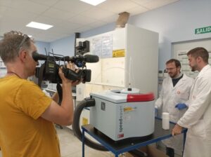 A man filming two researchers in a laboratory.