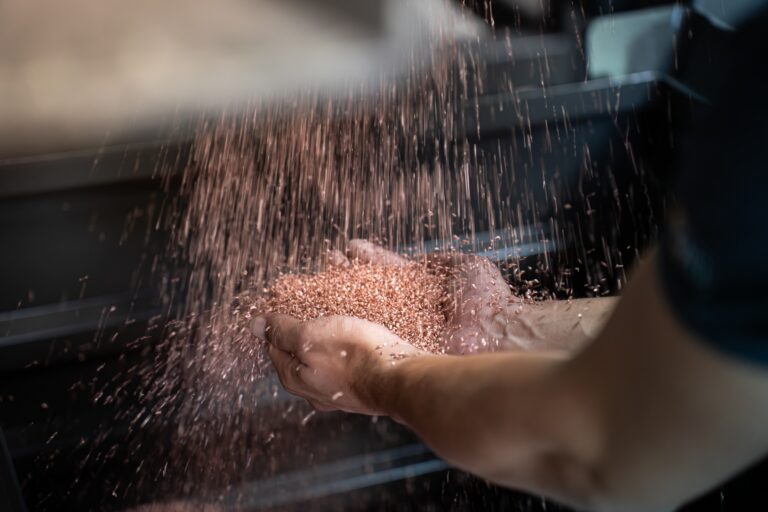 Shredded metal particles falling from a conveyor belt into a man's hands.