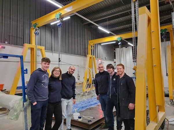Six people standing in a hall in front of industrial equipment.