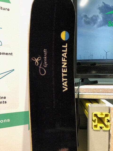 A black ski standing vertically against a wall. The logos Gjenkraft and Vattenfall are printed on the surface.