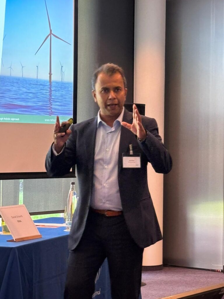 A man standing in front of a screen showing a picture of a wind turbine.
