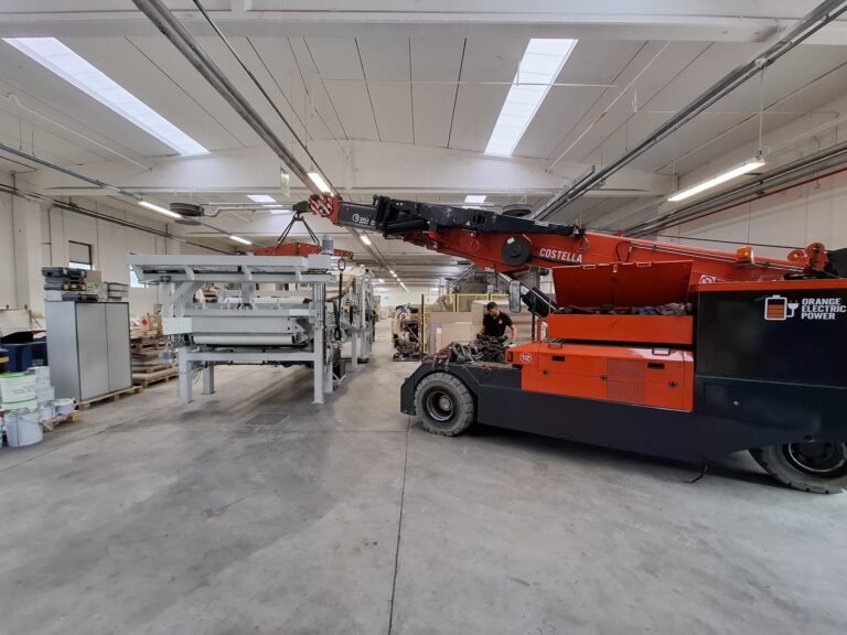A red vehicle moving a piece of equipment in a factory.