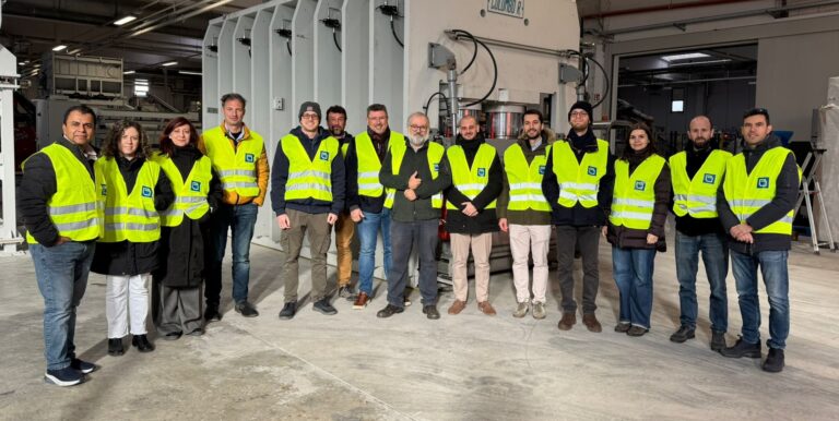 Group of people in yellow safety jackets in front of a big grey machine.