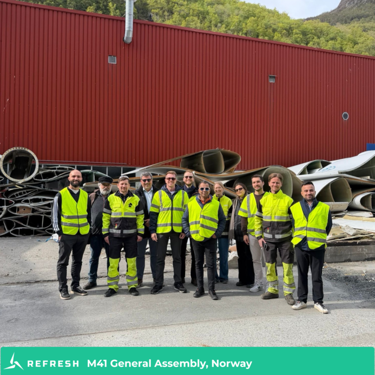 Group of people in yellow jackets in front of wind turbine blades.